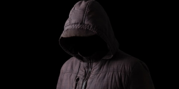 Mann versteckt sich im Dunkeln unter einer schwarzen Kapuze